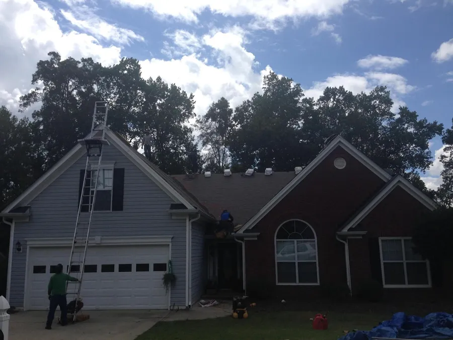 Roof work underway on a two-story home with a ladder up and tarps laid out