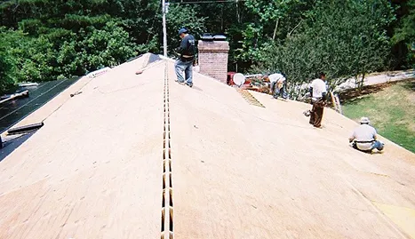 Crew working on bare roof decking with the ridge vent slot cut along the peak